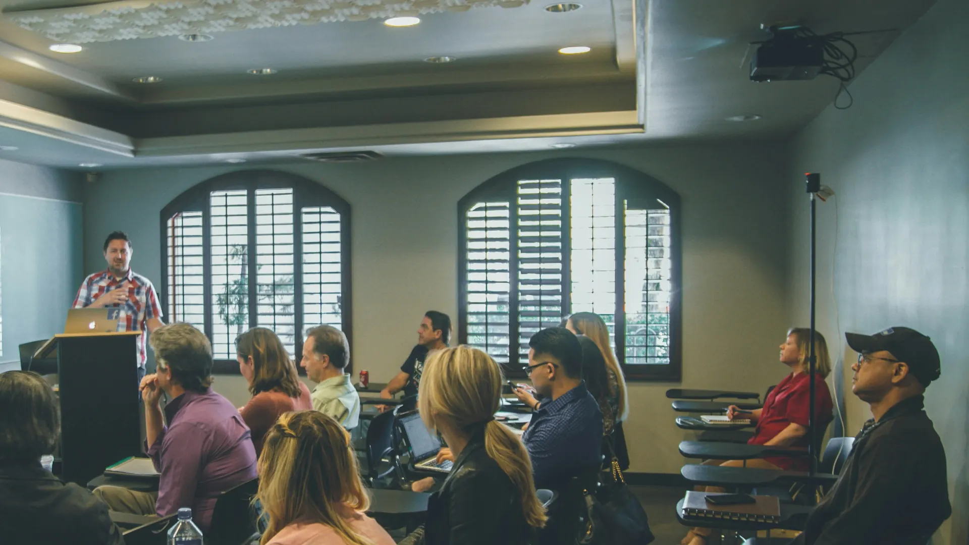 An instructor speaks with adults seated in a training classroom.